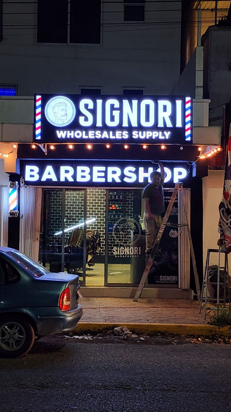 Fachada de barbería con letrero luminoso encendido de noche en Cancún
